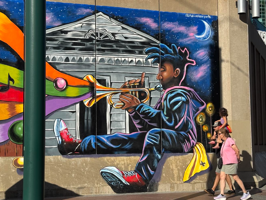A bright mural of a musician behind people walking by.